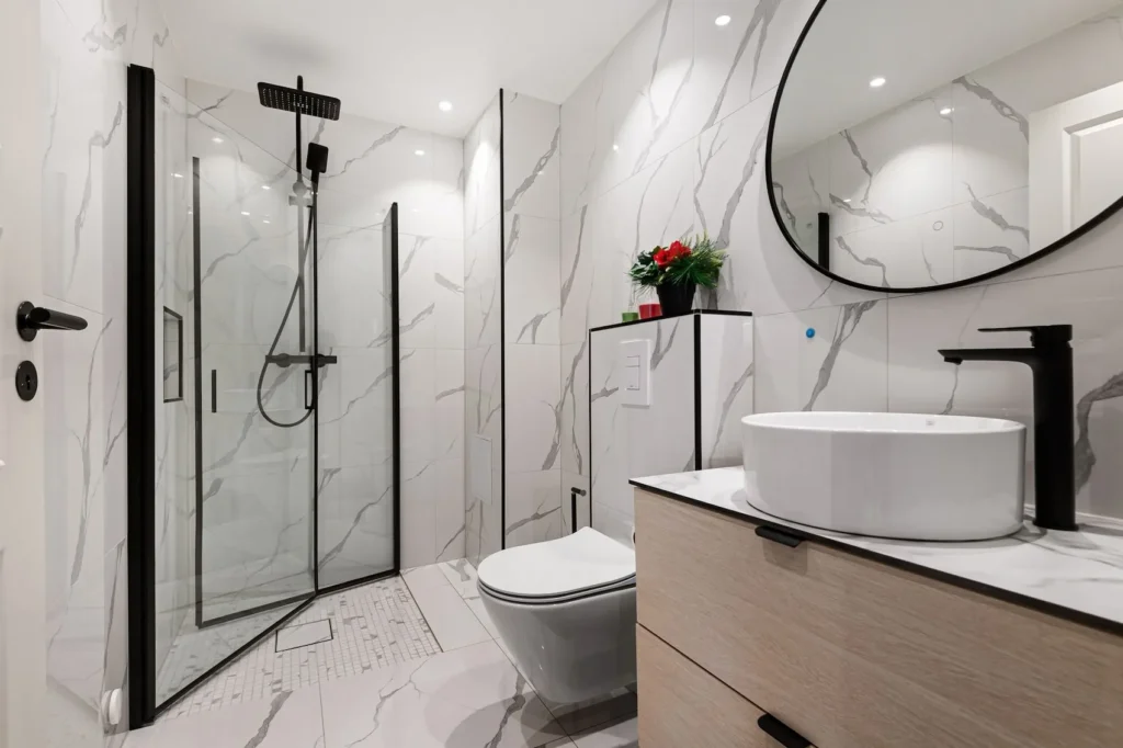 Modern luxury bathroom with white marble-effect floor and wall tiles, a glass shower cubicle, and a wooden vanity, showcasing a finished space where managing underfloor bathroom heating cost adds long-term value.